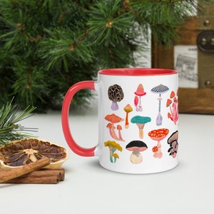 May include: White ceramic mug with a red rim, featuring a colourful illustration of various mushrooms. The mug is filled with a white liquid.
