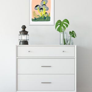 May include: A framed illustration of a cluster of gray mushrooms with yellow stems on a peach background. The mushrooms are surrounded by green foliage and small white dots.