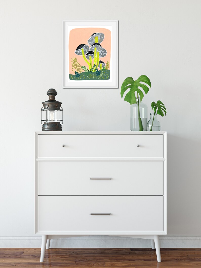 May include: A framed illustration of a cluster of gray mushrooms with yellow stems on a peach background. The mushrooms are surrounded by green foliage and small white dots.