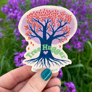May include: A sticker with a blue tree with red leaves and a green heart. The text "Tree Hugger" is written around the tree in green letters. The sticker is on a white background.