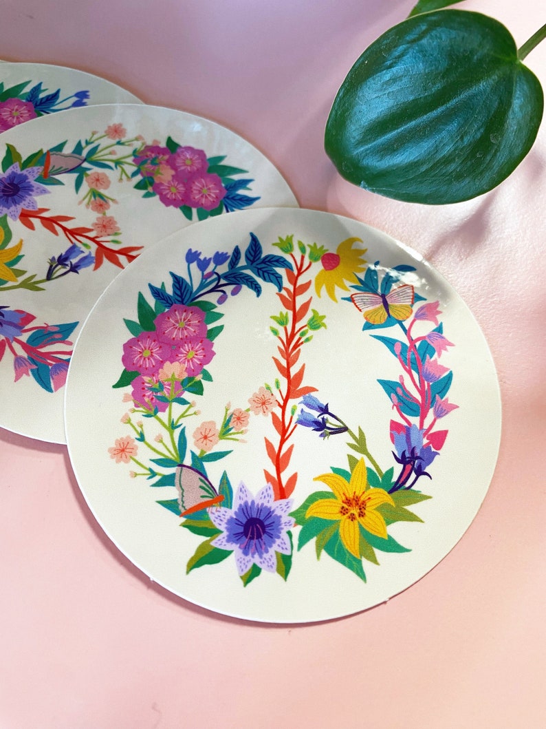 May include: A white round sticker with a peace sign design. The peace sign is made of colorful flowers, leaves, and butterflies. The sticker is perfect for adding a touch of whimsy to any surface.
