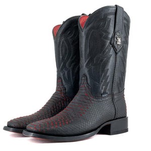 Op de afbeelding: Een paar zwarte cowboylaarzen met rode accenten. De laarzen hebben een textuurontwerp op het onderste deel en decoratieve stiksels op de bovenste schacht. De binnenvoering is rood.