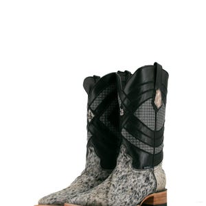 May include: A pair of cowboy boots with a spotted gray and white pattern on the foot and a black leather upper. The boots have a decorative design on the shaft and a wooden sole.