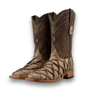 May include: Brown cowboy boots with a distinctive design. The boots have a fish-scale-like texture on the foot and an embossed pattern on the shaft. They feature a square toe and a stacked heel, showcasing a rustic aesthetic.