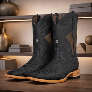 May include: A pair of black leather cowboy boots with a textured pattern and square toes. The boots have brown accents and a light brown sole. The boots are displayed on a wooden surface.