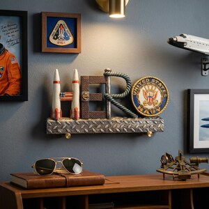 May include: A decorative wall display featuring the word "HERO" with rockets, a Navy emblem, and a framed astronaut portrait. Includes a model space shuttle and aviator sunglasses on a wooden desk. The color scheme includes blue, brown, and white.