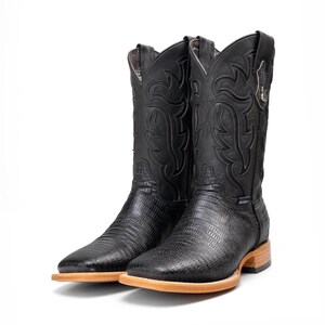 May include: A pair of black cowboy boots with a textured pattern on the vamp and shaft. The boots have a square toe and a light brown sole. The shaft features decorative stitching.