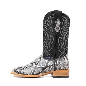May include: A single cowboy boot with a black leather upper and a snakeskin-patterned lower. The boot features decorative stitching and a square toe. The heel is made of light-colored wood. The brand name "Rockem" is visible on the boot.