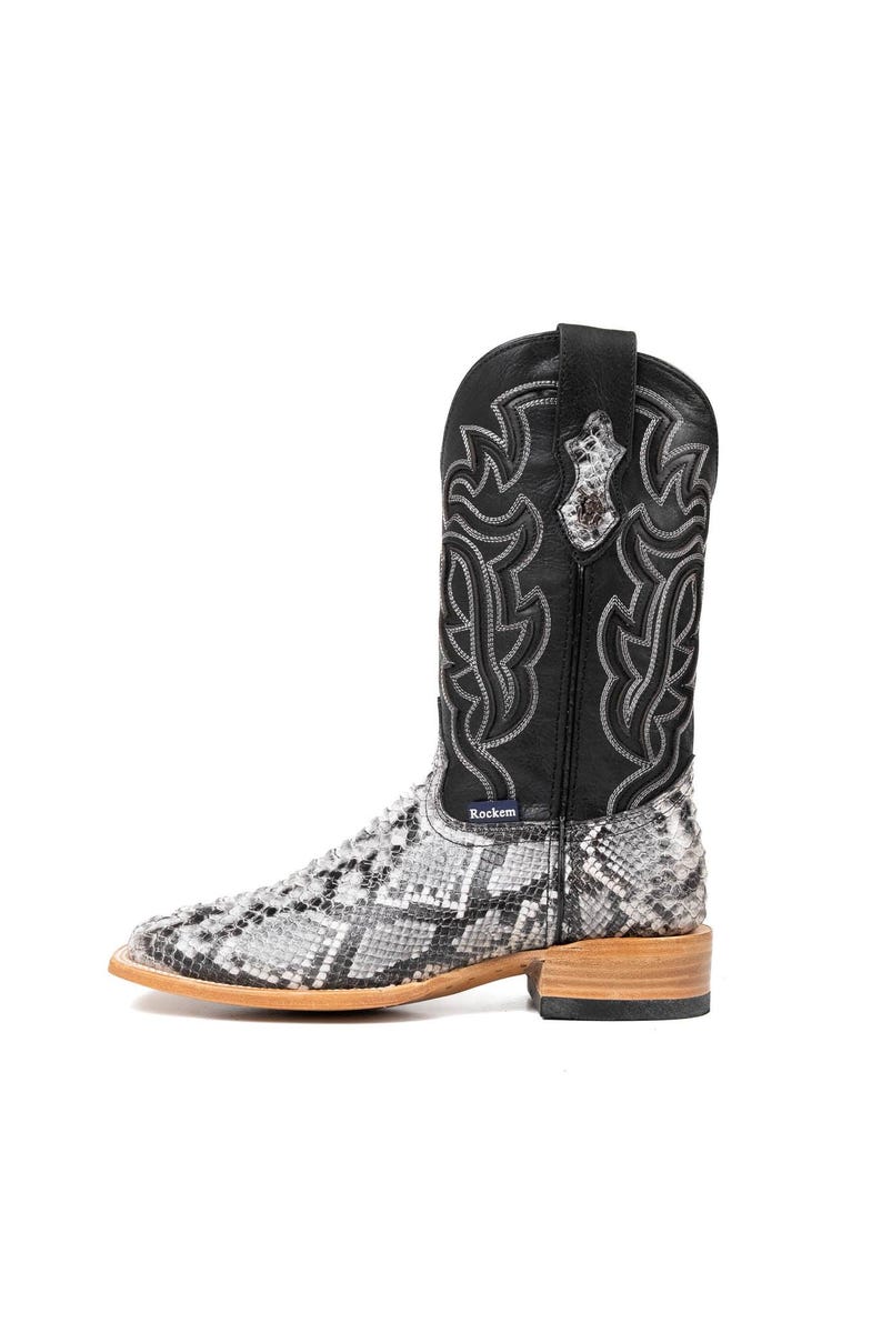 May include: A single cowboy boot with a black leather upper and a snakeskin-patterned lower. The boot features decorative stitching and a square toe. The heel is made of light-colored wood. The brand name "Rockem" is visible on the boot.