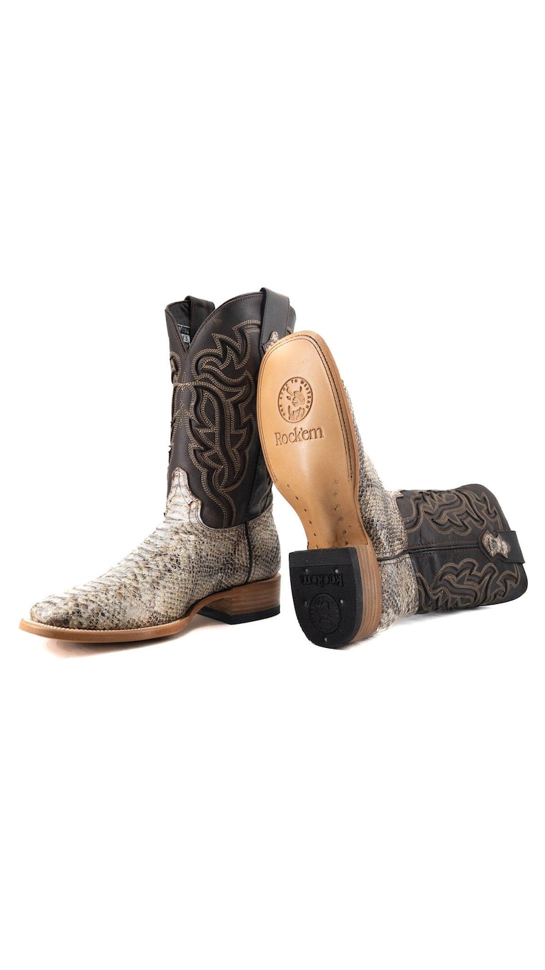 May include: A pair of cowboy boots with a snakeskin pattern on the foot and a dark brown leather upper. The boots have a square toe and decorative stitching. The soles are visible, with the brand name "Rock'em" printed on them.