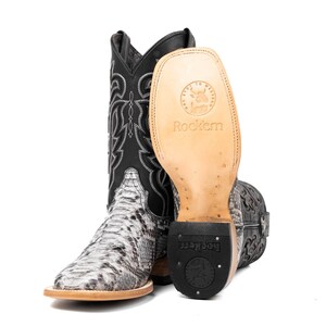 May include: A pair of cowboy boots with a snakeskin pattern on the foot and a black shaft with white stitching. The sole of one boot is visible, displaying the brand name "Rockem". The boots have a square toe and a stacked heel.
