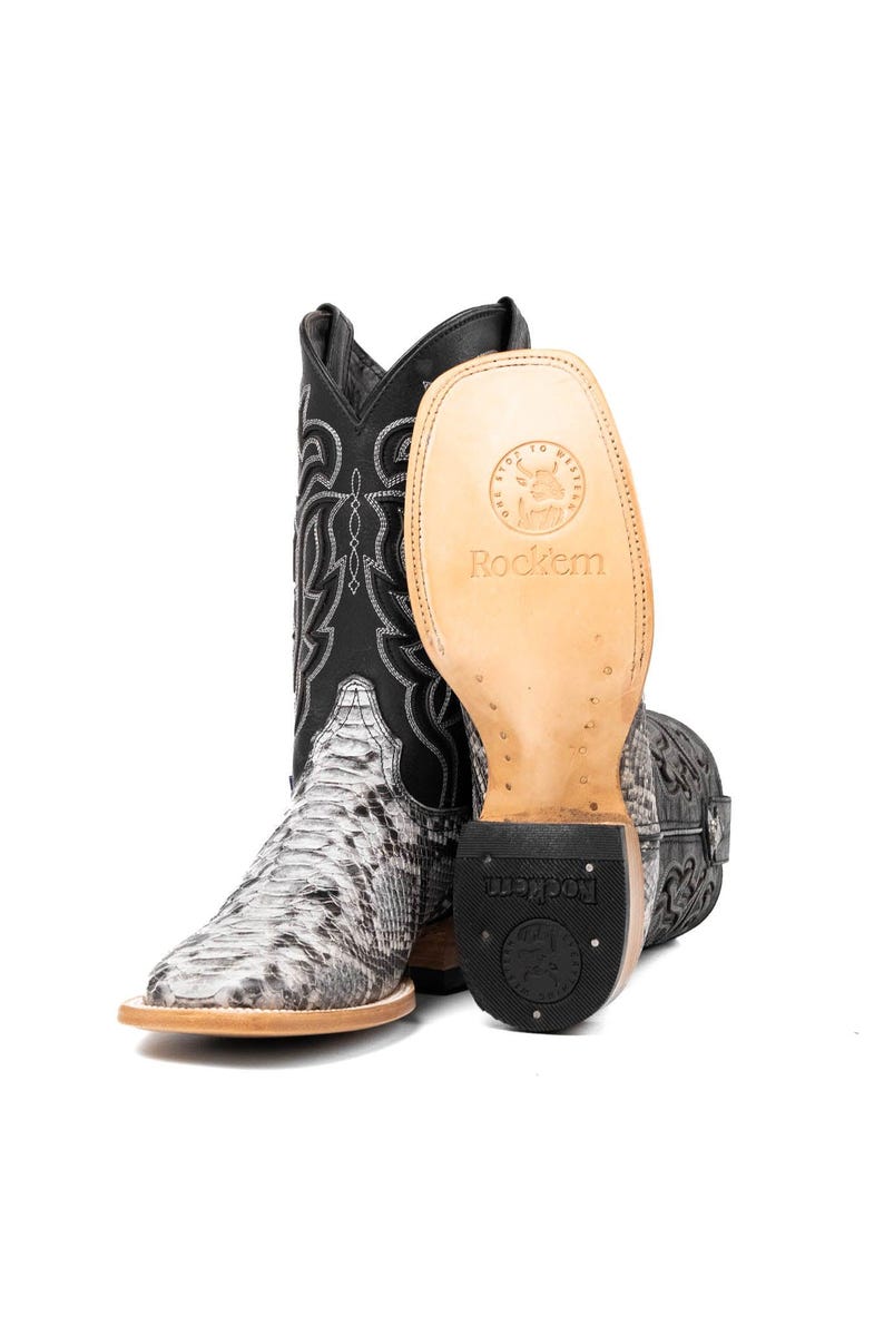 May include: A pair of cowboy boots with a snakeskin pattern on the foot and a black shaft with white stitching. The sole of one boot is visible, displaying the brand name "Rockem". The boots have a square toe and a stacked heel.