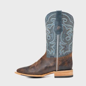 May include: Brown and blue cowboy boot with decorative stitching. The boot has a square toe, a stacked heel, and a leather upper. The shaft is blue with turquoise and brown stitching. The foot of the boot is brown leather.