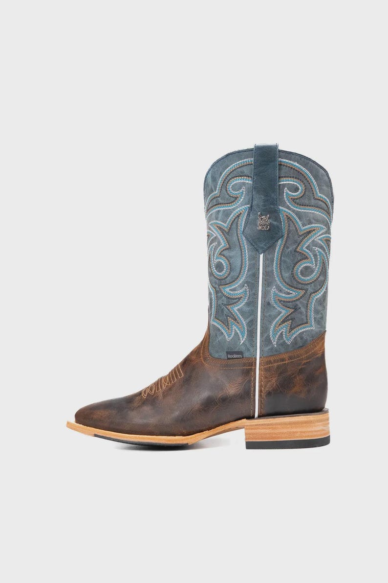 May include: Brown and blue cowboy boot with decorative stitching. The boot has a square toe, a stacked heel, and a leather upper. The shaft is blue with turquoise and brown stitching. The foot of the boot is brown leather.