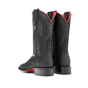 May include: Black cowboy boots with a textured pattern and red accents. The boots have a square toe and a red sole. The interior lining is red. The boots are set against a white background.