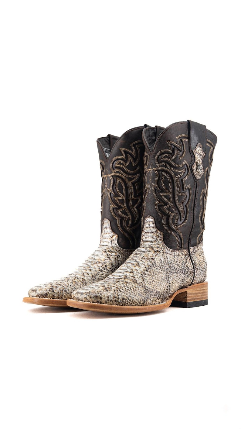 May include: A pair of cowboy boots with a snakeskin pattern on the foot and a dark brown leather upper. The boots have decorative stitching and a square toe. The soles are light brown.