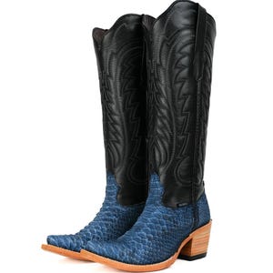 May include: A pair of cowboy boots with a black leather upper and a blue, textured lower section. The boots have a pointed toe and a wooden heel. The design features decorative stitching on the black leather.