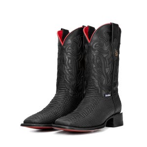 Op de afbeelding: Een paar zwarte cowboylaarzen met een textuurpatroon en rode accenten. De laarzen hebben een vierkante neus en een decoratief ontwerp op de schacht. De binnenkant en de zool zijn rood.