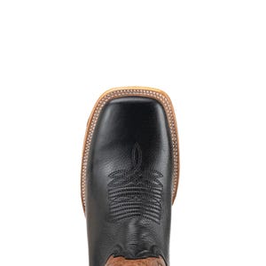 May include: Overhead shot of a black leather cowboy boot with a square toe. The boot has decorative stitching on the vamp and a light brown sole. The upper part of the boot is black, and the sole is light brown.