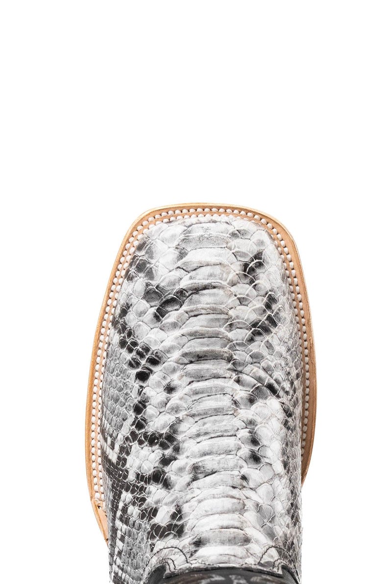 May include: Close-up of a square-toe boot with a snakeskin pattern in shades of gray and black. The boot has a light brown leather trim around the toe and a light brown sole.