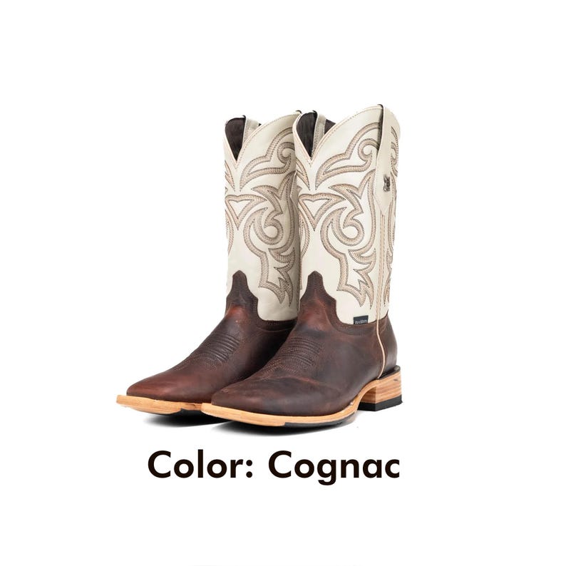 May include: A pair of cognac-coloured cowboy boots with cream-coloured shafts featuring intricate stitching. The boots have a square toe and a light-coloured sole. The text "Color: Cognac" is displayed below the boots.