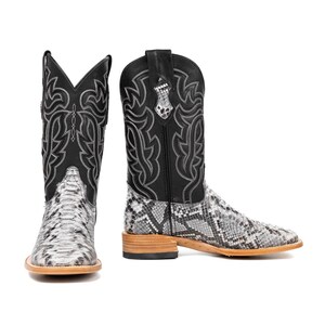 May include: A pair of cowboy boots with a snakeskin pattern on the foot and a black leather upper. The boots have decorative stitching and a square toe. The soles are a light brown color.