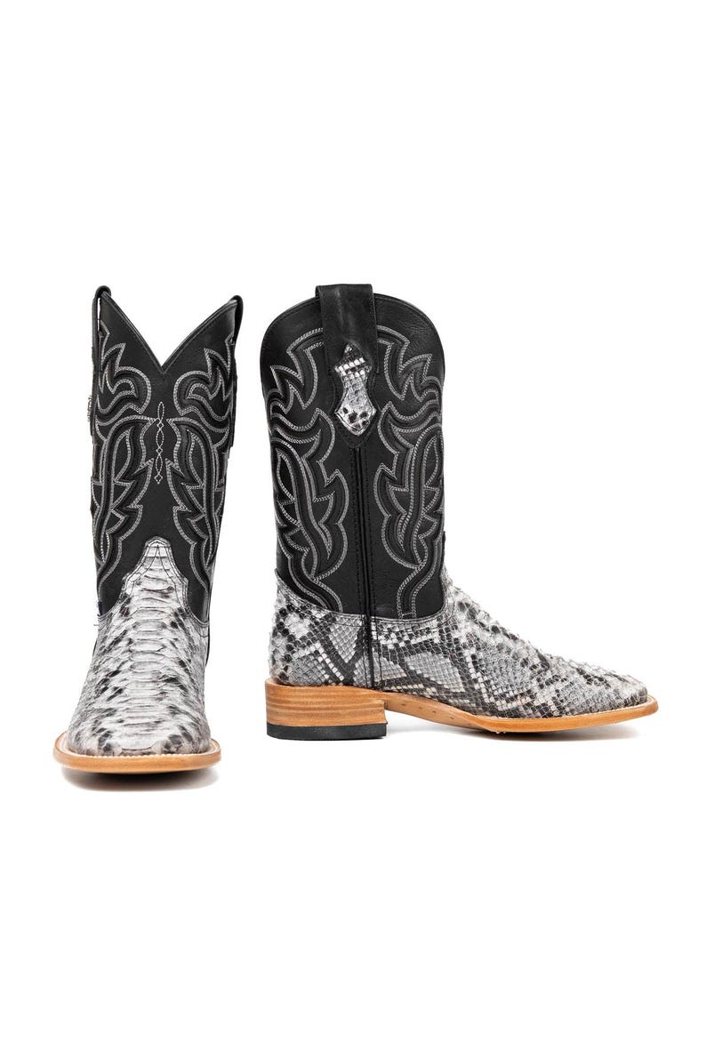 May include: A pair of cowboy boots with a snakeskin pattern on the foot and a black leather upper. The boots have decorative stitching and a square toe. The soles are a light brown color.