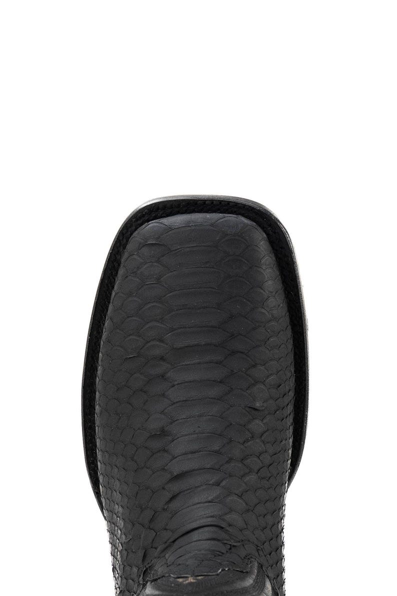 May include: Close-up of a black leather boot with a square toe. The boot features a textured, scale-like pattern across the surface. The top edge of the boot is smooth and black.