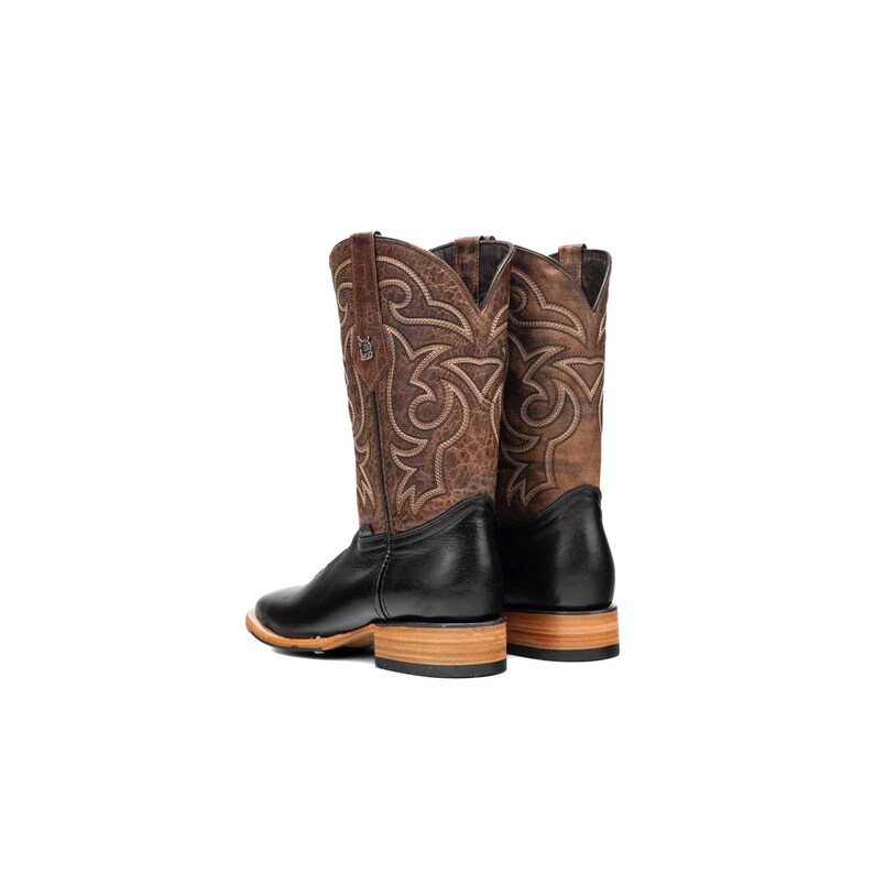 May include: A pair of brown and black cowboy boots. The boots feature a square toe, a black leather foot, and a brown leather upper with decorative stitching. The heel is made of light-coloured wood. The boots are set against a white background.