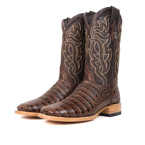 May include: A pair of brown leather cowboy boots with a square toe and intricate stitching. The boots feature a crocodile-like texture on the foot and a decorative pattern on the shaft. The heel is a light brown color.