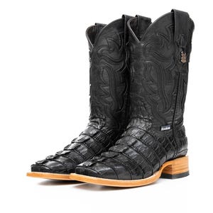 Pode incluir: Um par de botas de cowboy pretas com um padrão texturizado, semelhante ao de um crocodilo, no pé e na haste. As botas têm bico quadrado, sola de cor clara e costuras decorativas. A marca "Rockin" é visível.
