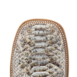May include: Close-up of a western-style boot toe. The boot features a snakeskin pattern in shades of gray, brown, and cream. The toe is square with a light brown leather trim and a decorative stitch pattern.