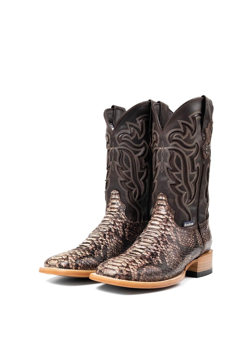 May include: A pair of brown and tan cowboy boots with a snakeskin pattern on the foot and a decorative stitched design on the upper shaft. The boots have a square toe and a stacked heel.