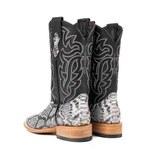 May include: A pair of black cowboy boots with a snakeskin pattern on the lower part and a decorative stitched design. The boots have a square toe and a wooden sole.