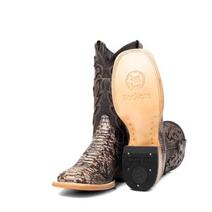 May include: Brown and tan cowboy boots with a snakeskin pattern on the foot and decorative stitching on the shaft. The sole of one boot is visible, displaying the brand name "Rockem".