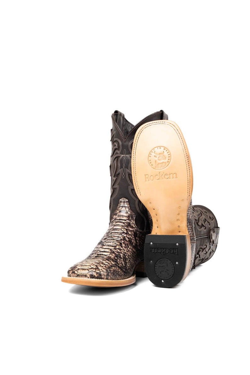 May include: Brown and tan cowboy boots with a snakeskin pattern on the foot and decorative stitching on the shaft. The sole of one boot is visible, displaying the brand name "Rockem".