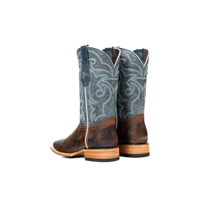May include: A pair of cowboy boots with a square toe. The boots have a distressed brown leather foot and a blue shaft with a decorative pattern. The shaft is accented with white stitching and a blue leather pull tab.