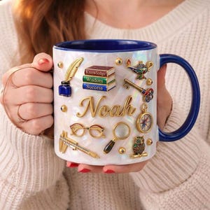 May include: A set of three ceramic mugs with a speckled, cream-colored glaze. Each mug features a different hand-painted design: a blue and green leaf, a yellow flower, and a red berry. The mugs have a simple, rounded shape.