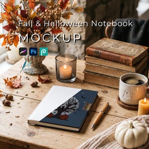 May include: A notebook with a white and dark blue cover featuring a tree, bats, and pumpkin graphic. The text Fall & Halloween Notebook MOCKUP is visible. Nearby are a pen, a stack of books, a mug with a ghost, candles, and a white pumpkin.