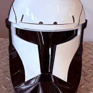 May include: A black and white helmet with a visor. The helmet has a white top and faceplate with black accents. The visor is black, and the helmet appears to be made of plastic or a similar material. The helmet is likely a costume or cosplay item.