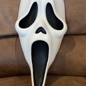 Puede incluir: Una máscara blanca de Scream con aberturas negras para los ojos y la boca. La máscara tiene una forma curva con una boca larga y abierta. Las aberturas de los ojos tienen un material de malla. Un accesorio de disfraz de Halloween clásico.
