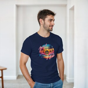 Puede incluir: Camiseta azul marino con un dise&ntilde;o gr&aacute;fico circular que representa una puesta de sol, palmeras y la frase "Beach Vibes". El dise&ntilde;o utiliza colores vibrantes como naranja, rosa y azul.