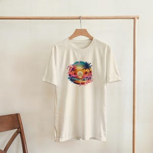 Puede incluir: Camiseta de color crema con un gr&aacute;fico circular vibrante de una puesta de sol sobre el oc&eacute;ano con palmeras. El gr&aacute;fico incluye el texto "Aloha" en una fuente estilizada. La camiseta est&aacute; colgada en una percha de madera.