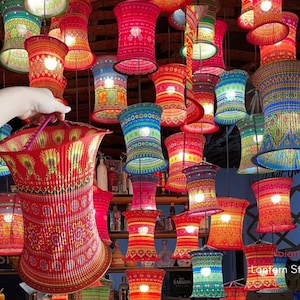 Könnte beinhalten: Eine Sammlung farbenfroher, gemusterter Pendelleuchten in verschiedenen Größen und Designs. Die Lampen sind hauptsächlich rot, blau, grün und orange, mit aufwendigen Mustern. Eine Lampe wird von einer Hand gehalten. Das Bild stammt von Lantern Studio.