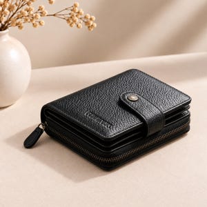 May include: A black bi-fold wallet with a textured, pebbled surface. The wallet features a snap-button closure with a metallic finish and a wrap-around zipper with a matching black pull tab. The brand name CHUANNA is embossed on the front flap.