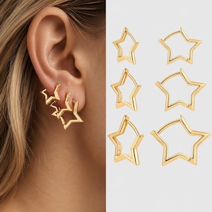 Puede incluir: Pendientes dorados en forma de estrella. Los pendientes se muestran en múltiples estilos, incluyendo un diseño de triple estrella y aros de estrella individuales. Los pendientes se muestran en una oreja y sobre un fondo blanco.