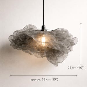 May include: A grey, cloud-shaped pendant light. The light is approximately 38 cm wide and 25 cm tall. The fixture is made of a mesh material and has a single light bulb. The text "NeleForm - Drift 01" is at the top.