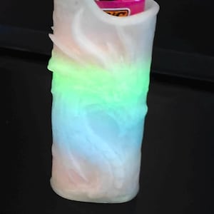 May include: A cylindrical, white, textured lighter holder with a color-changing LED light. The light transitions from pink to blue to green. A pink and black lighter is visible inside the holder.