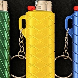 May include: Three lighters in green, yellow, and blue, each encased in a textured holder with a keychain attachment. The lighters have a red ignition button and a silver metal top.