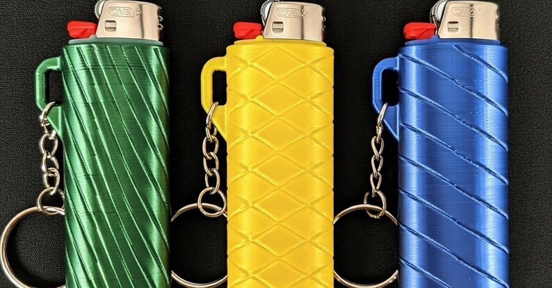 May include: Three lighters in green, yellow, and blue, each encased in a textured holder with a keychain attachment. The lighters have a red ignition button and a silver metal top.
